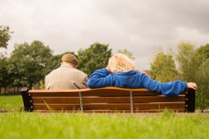 A woman sits beside an older man on a bench in a park, talking about what he’s struggling with and how to get back on track.