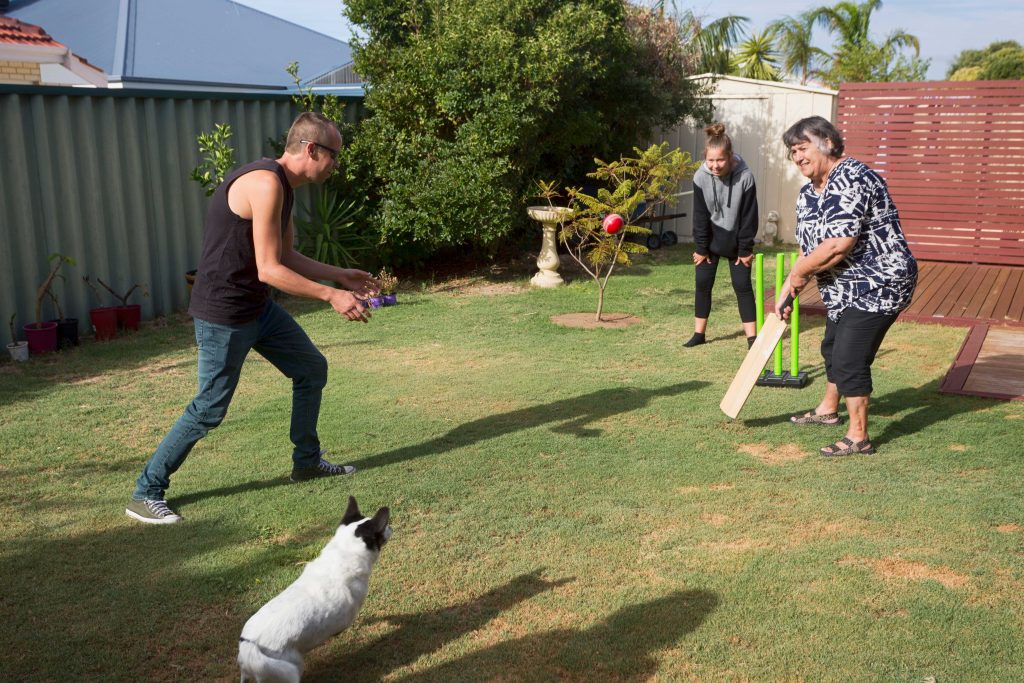 Family, including grandmother, playing backyard cricket