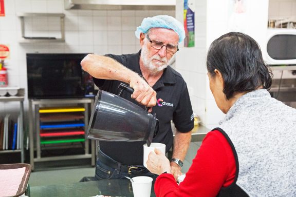 A volunteer at Chorus Kitchen pours a cup of tea for a customer