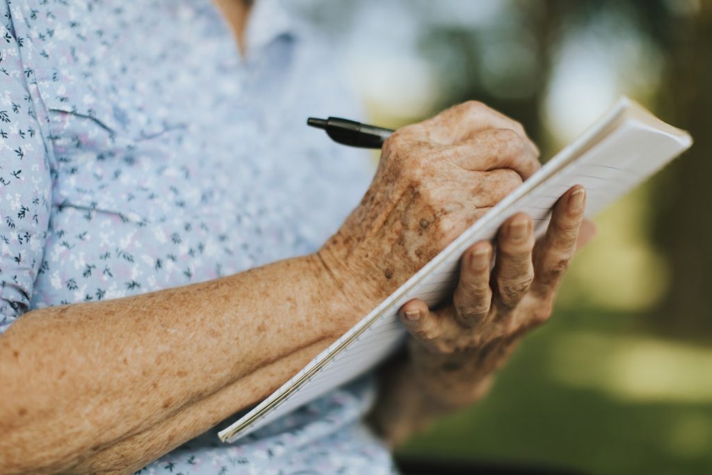 Older Person's Hands Writing on Notepad